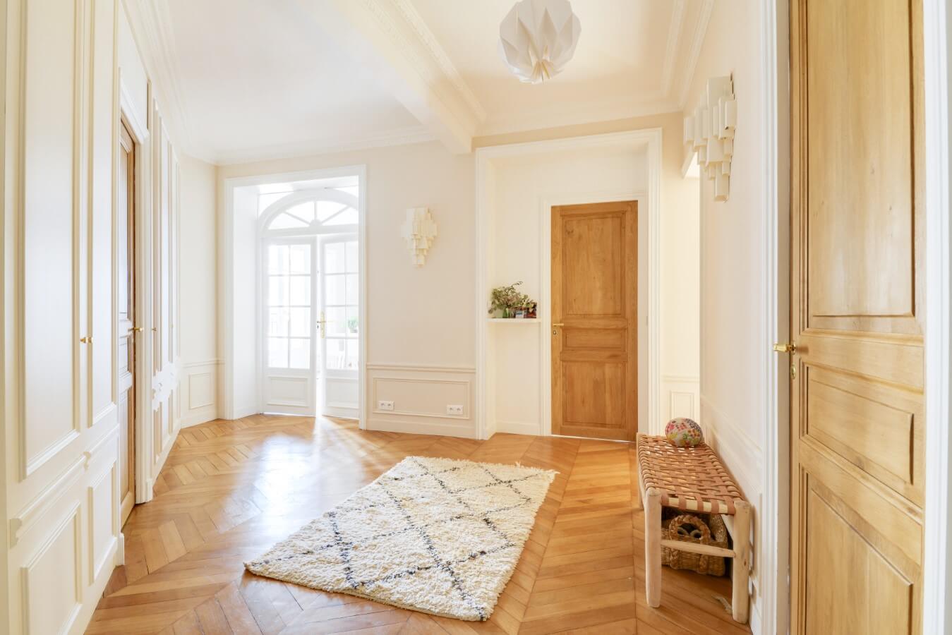 Entrée haussmannienne de l'appartement avec porte vitrée parquet chevron