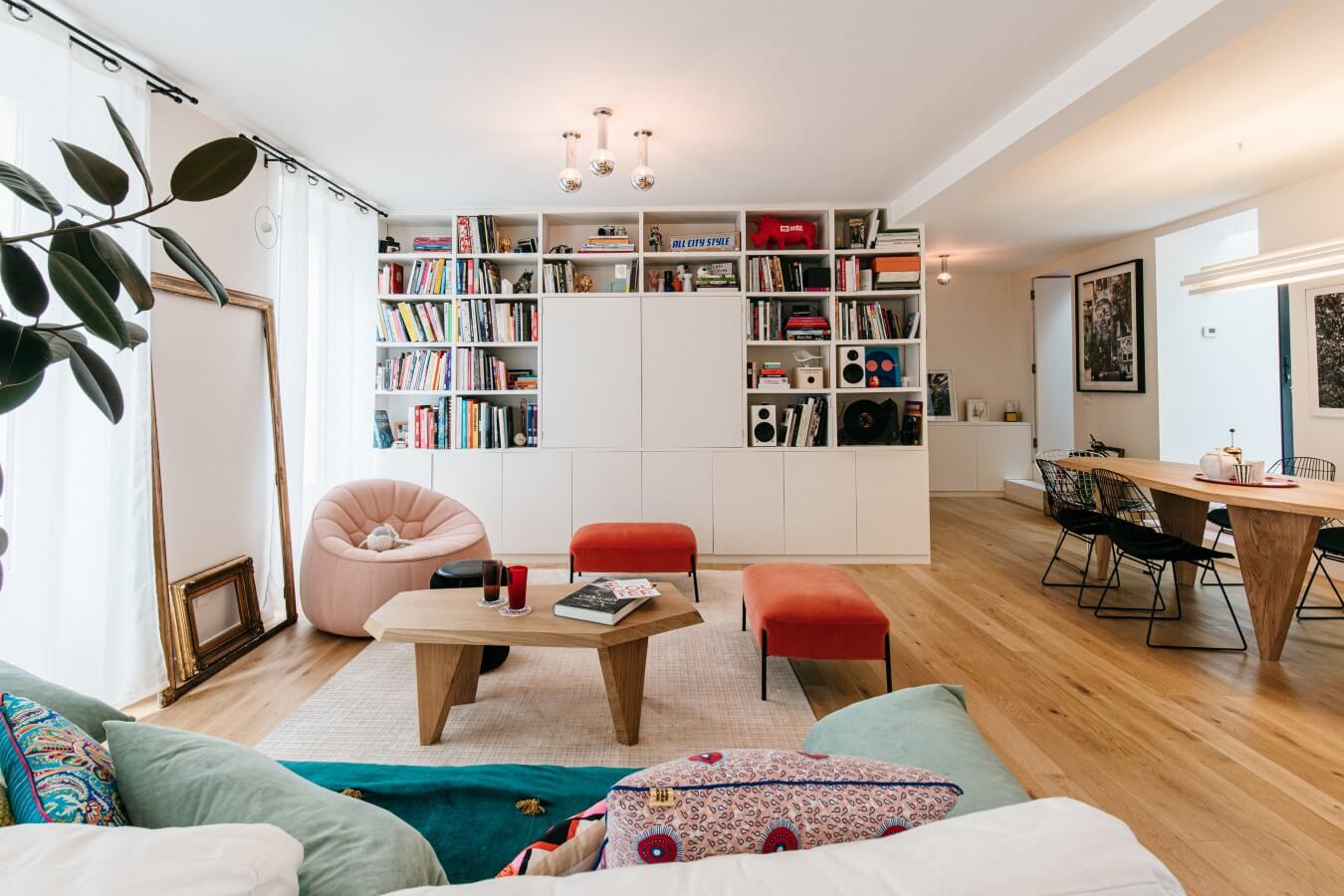 Salon familial coloré avec parquet massif, un grand meuble télé bibliothèque, table sur-mesure. fauteuil et pouf Cina, table Guillemette Paris