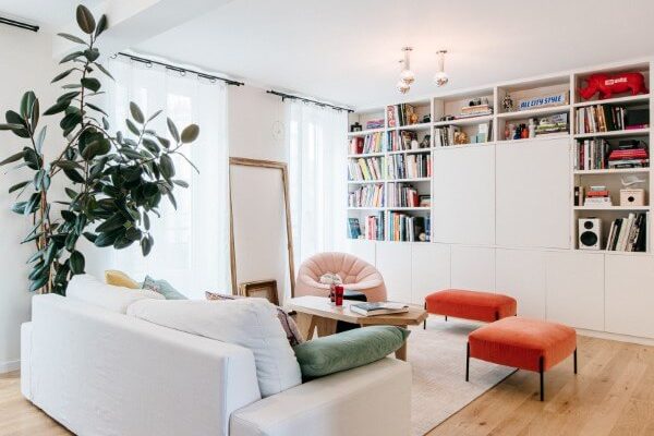 Salon familial coloré avec parquet massif, un grand meuble télé bibliothèque, table sur-mesure. fauteuil et pouf Cina, table Guillemette Paris