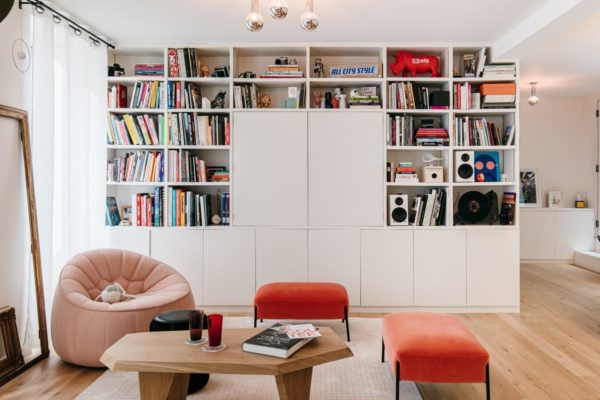 Salon familial coloré avec parquet massif, un grand meuble télé bibliothèque, table sur-mesure. fauteuil et pouf Cina, table Guillemette Paris