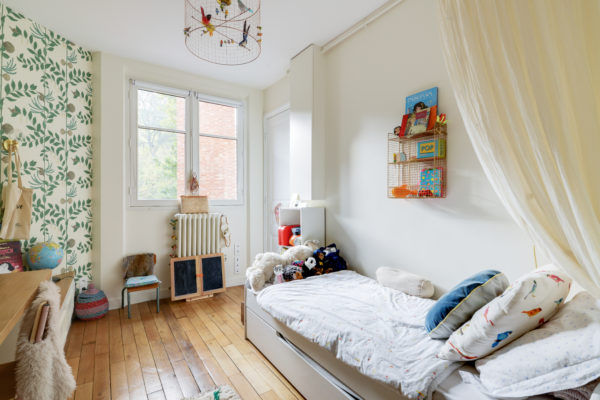 Une ancienne cuisine transformée en chambre d'enfant. Le béton ciré a été recouvert de parquet massif, des rangements et un coin bureaux ont été conçus et ont atmosphère douce et chaleureuse c'est installé dans cet espace aux touches végétales et scandinaves. Au plafond la lampe volière de Mathieu Challières