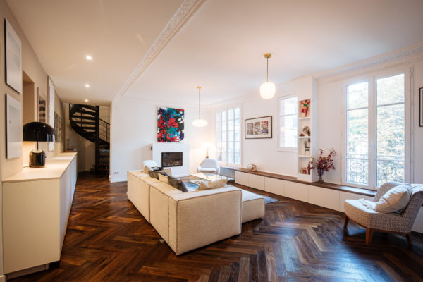 Salon d'un duplex entièrement rénové par l'agence d'architecture U design Paris. Un canapé Sia et des fauteuils Eichholtz en bouclette blanche accompagnés d'un Tapis Idaho edition et d'une table basse en verre de chez Akante. Au fond un tableau de Agathe de Bailliencourt