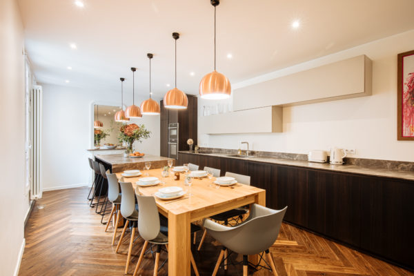 Œuvre d'art d'Hendrick accrocher dans la cuisine d'un duplex entièrement rénové par l'agence d'architecture U design Paris. Remplacement d'un parquet chevron et installation d'un mobilier de rangement beige associé à un bois sombre et à du marbre noir. Au centre une table en bois et un plan de travail avec d'un côté des rangements et de l'autre des tabourets pour s'installer