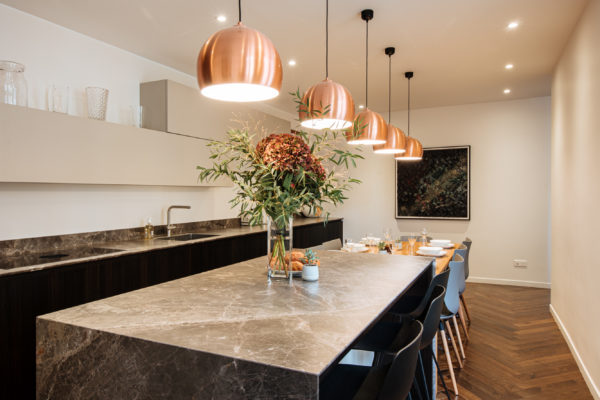 Œuvre d'art d'Hendrick accrocher dans la cuisine d'un duplex entièrement rénové par l'agence d'architecture U design Paris. Remplacement d'un parquet chevron et installation d'un mobilier de rangement beige associé à un bois sombre et à du marbre noir. Au centre une table en bois et un plan de travail avec d'un côté des rangements et de l'autre des tabourets pour s'installer