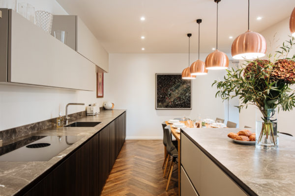 Œuvre d'art d'Hendrick accrocher dans la cuisine d'un duplex entièrement rénové par l'agence d'architecture U design Paris. Remplacement d'un parquet chevron et installation d'un mobilier de rangement beige associé à un bois sombre et à du marbre noir. Au centre une table en bois et un plan de travail avec d'un côté des rangements et de l'autre des tabourets pour s'installer