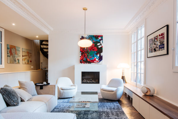 Salon d'un duplex entièrement rénové par l'agence d'architecture U design Paris. Un canapé Sia et des fauteuils Eichholtz en bouclette blanche accompagnés d'un Tapis Idaho edition et d'une table basse en verre de chez Akante. Au fond un tableau de Agathe de Bailliencourt