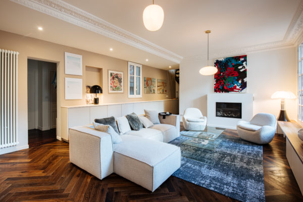 Salon d'un duplex entièrement rénové par l'agence d'architecture U design Paris. Un canapé Sia et des fauteuils Eichholtz en bouclette blanche accompagnés d'un Tapis Idaho edition et d'une table basse en verre de chez Akante. Au fond un tableau de Agathe de Bailliencourt