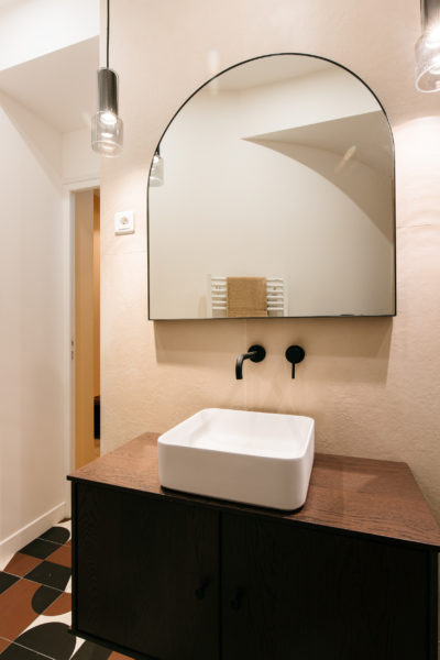 Salles de bain au miroir en arc de cercle, robinetterie noire, plan de travail en bois et carrelage Mutina. Rénovation par l'agence U design Paris